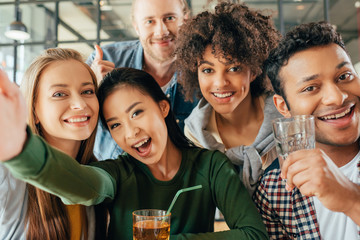 Young happy multiethnic friends taking selfie in cafe