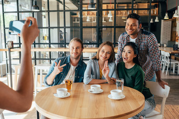 Young woman taking photo of multiethnic friends resting in cafe