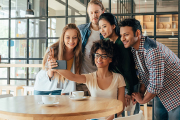 Young happy multiethnic friends taking selfie in cafe