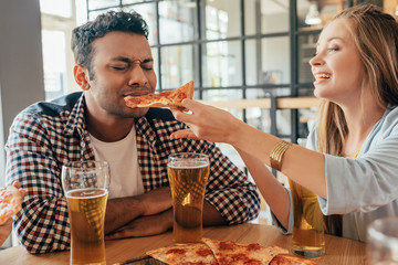 Young woman feeding her boyfriend during date in pizzeria