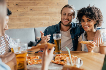 Young smiling interracial couple spending time together with friends in cafe