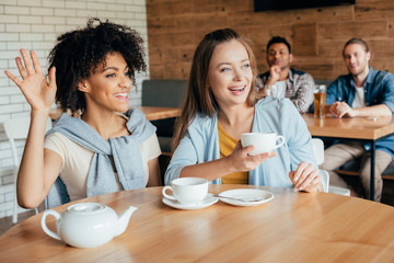 Two young women having tea in cafe and men sitting at next table looking at them