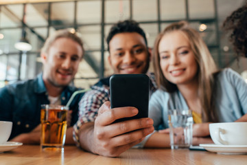 Young happy multiethnic friends taking selfie in cafe