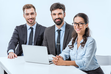 portrait of smiling business people looking at camera while sitting at workplace with laptop