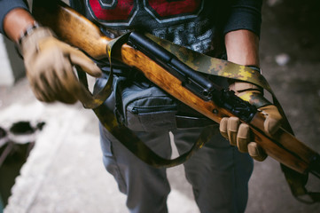 Athletic man in gray clothes with a carbine gun in his hand. Close-up of tactical gloves with weapons