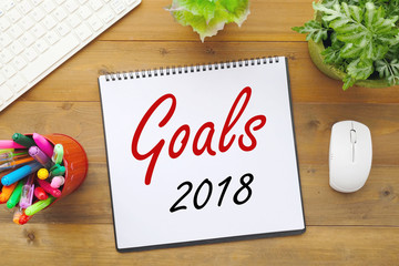 2018 goals on paper note book background on office table, business and new year concept
