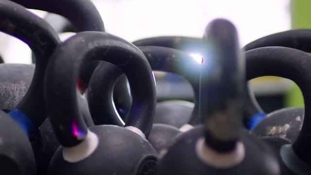 PAN with lens flare of row of cast-iron kettlebells standing in empty gym on sunny day