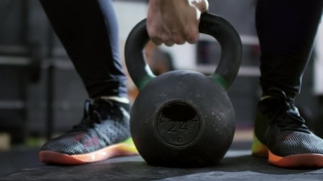 PAN with mid-section of unrecognizable sportswoman standing on step and doing kettlebell swings 