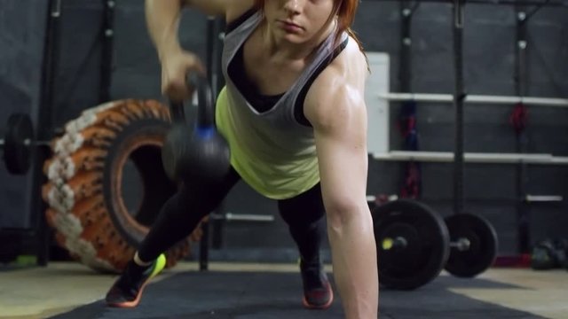 Zoom in of strong sportswoman with big muscles doing single arms kettlebell rows