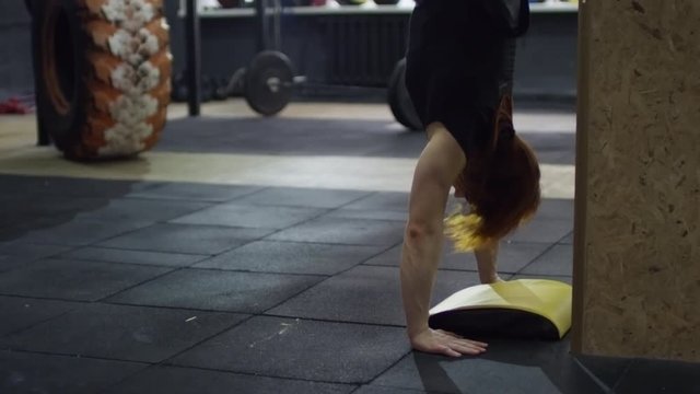 Tilt up of muscular female athlete performing handstand push-ups during cross-training routine in gym