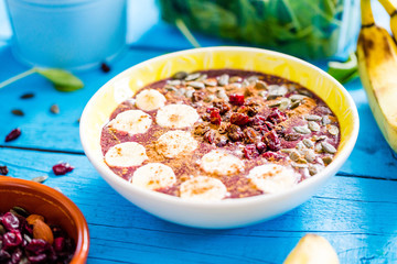Close-up View of Blueberry Smoothie Bowl with Banana, Pumpkin Seeds, Cinnamon and Cranberries on Blue Wooden Table