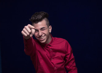 one teenager boy, red shirt, Caucasian, dark background, looking to camera, smiling, pointing finger to camera
