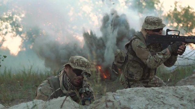 Group of men sniping while hiding behind in ambush in field surrounded with smoke,