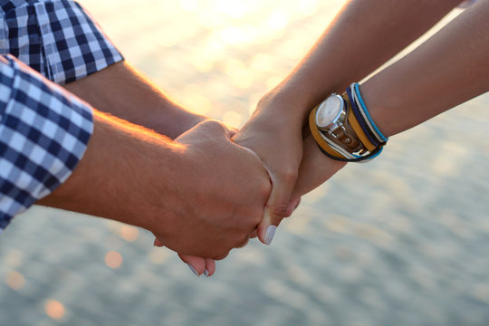 Two lovers (guy and girl) hold hands tightly on the beach.