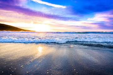 Small ocean sea waves on sandy beach with sunrise sunset.