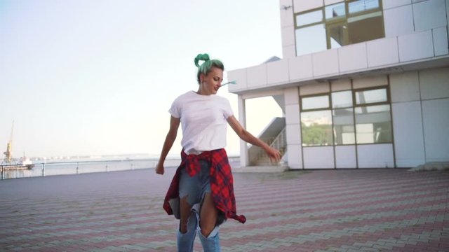 Attractive young woman in a stylish look and green hair dancing freely on urban background, slow motion