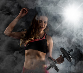 Fitness young woman in training with dumbbells, sporty muscular female brunette in smoke