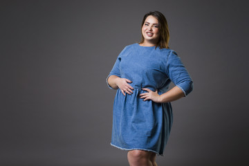 Plus size fashion model in casual jeans clothes, fat woman on gray background, overweight female body