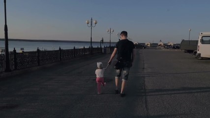 The father and his little daughter are holding hands along the embankment. Slow motion