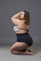 Plus size fashion model in sexy swimsuit, young fat woman on gray background, overweight female body