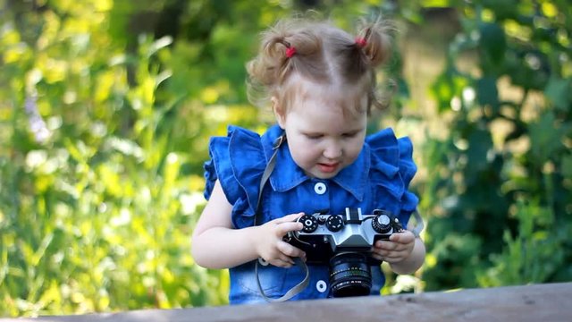 Funny curious baby girl is holding and photographing retro camera