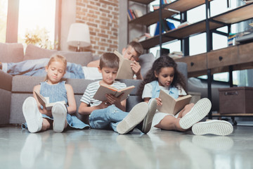 multicultural group of concentrated children reading books at home together