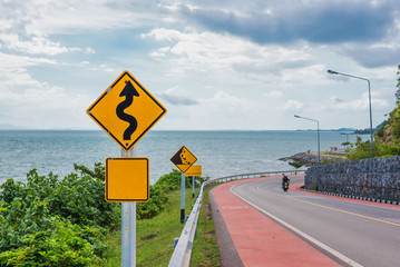 Yellow sign with winding road symbol in the countryside sea and sky background . - 165568566