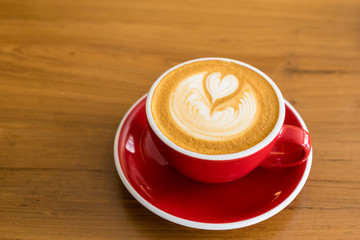 Red Coffee cup with heart shape latte art on wood table at café, Selective focus.