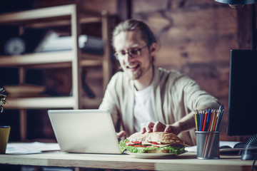 Man working at home going to eat at working place. Freelancer drawing hand to grab sandwich.