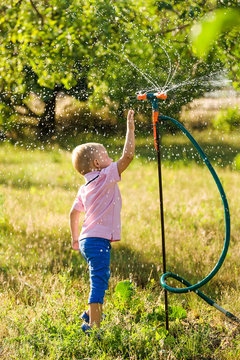 A boy play with water sprinkler in the summer garden
