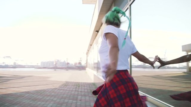 Attractive young woman in a stylish look and green hair dancing freely on urban background, slow motion