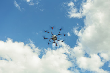 Hovering drone flies in blue sky and taking pictures of green hills. Professional agriculture drone flying in clear blue. Sky partly clouded