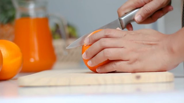 Close up shot hands of woman using kitchen knife to slash cut fresh and ripe orange on wood cutting board shallow depth of field
