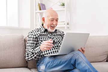 Smiling senior man reading news on laptop