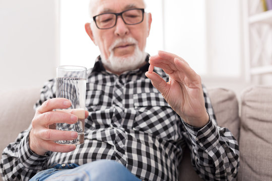 Old man having a glass of water and pills in hand