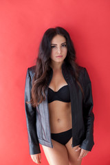 brunette girl in leather jacket and black lingerie on a red background