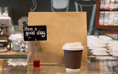 close up cup of coffee and brown paper bag in restaurant background. Takeaway, take out