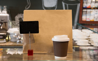 close up cup of coffee and brown paper bag in restaurant background. Takeaway, take out