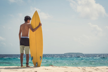 A young man standing with his surfboard on beach