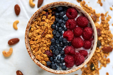 Bowl of homemade granola with yogurt and fresh berries decorated with nuts, oats and dried fruits on white background. Close up view. Collection