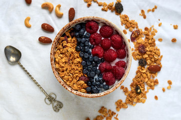 Bowl of homemade granola with yogurt, fresh berries and spoon decorated with nuts, oats and dried fruits on white background. Top view. Collection