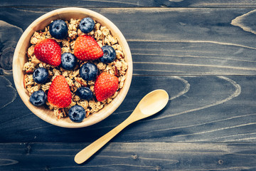 Homemade granola with strawberry and fresh berries on wood table.