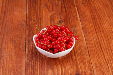 Red currants in ceramic bowl on wood background