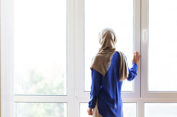 Muslim girl standing with her back against the window