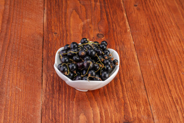 Black currants in ceramic bowl on wood background