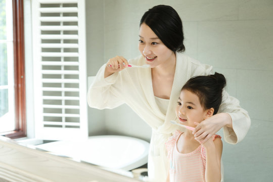 Mother teaching daughter brushing teeth