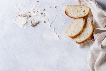 Homemade white wheat bread slice served with flour and wheat grain seeds on white linen towel over gray texture background. Top view with space.