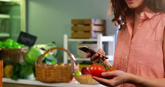 Woman holding tomato and using mobile phone