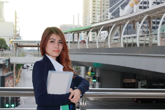 Portrait of young attractive Asian business woman standing and holding ring binder at the downtown city background.