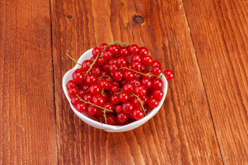 Red currants in ceramic bowl on wood background